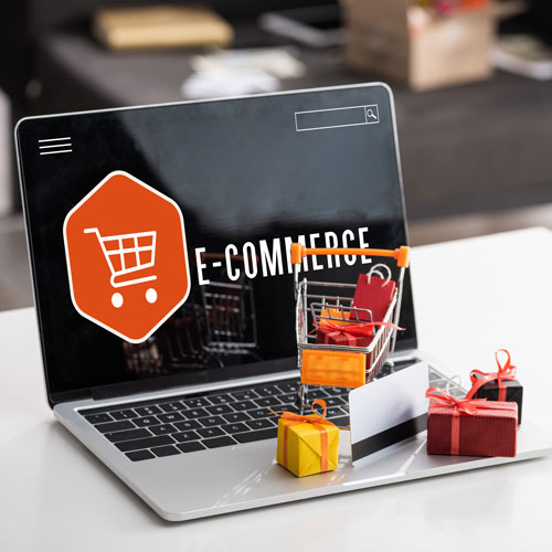 Laptop displaying an e-commerce screen with a shopping trolley icon, small gift boxes, and a miniature shopping trolley placed on the keyboard—ideal imagery for a black-owned digital marketing agency in South Africa. - Proudly Developing