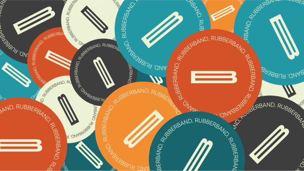 Overlapping red, teal, orange, and beige circles with a white elastic band graphic in the centre and “RUBBERBAND. RUBBERBAND.” text around the edges of each circle create a vibrant visual inspired by Rubberband Communications’ signature style. - Proudly Developing