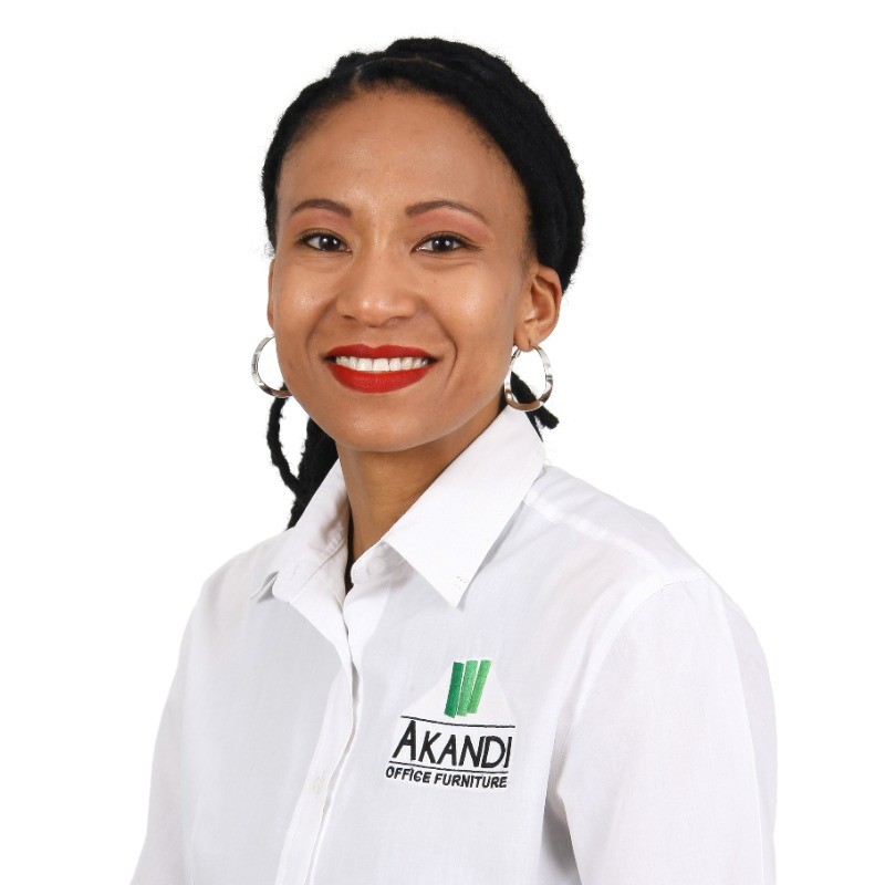 Woman wearing a white shirt with “Akandi Office Furniture” logo, smiling at the camera against a plain white background. - Proudly Developing